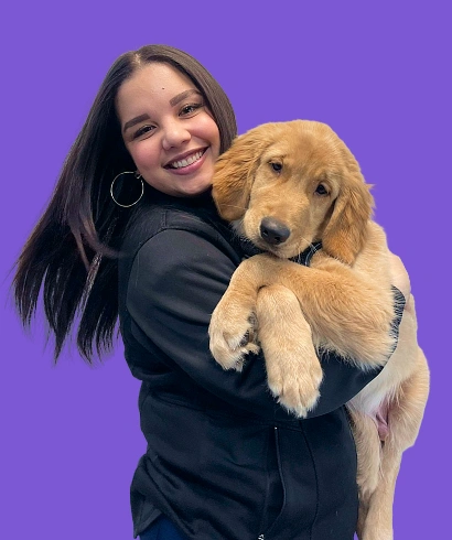 Dra. Yisenia Nazario smiling and holding a golden retriever puppy against a purple background